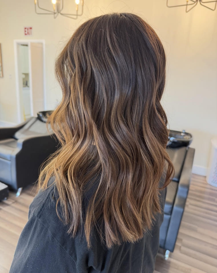 Mid-length brunette with caramel balayage and beachy waves, colored by Lauren